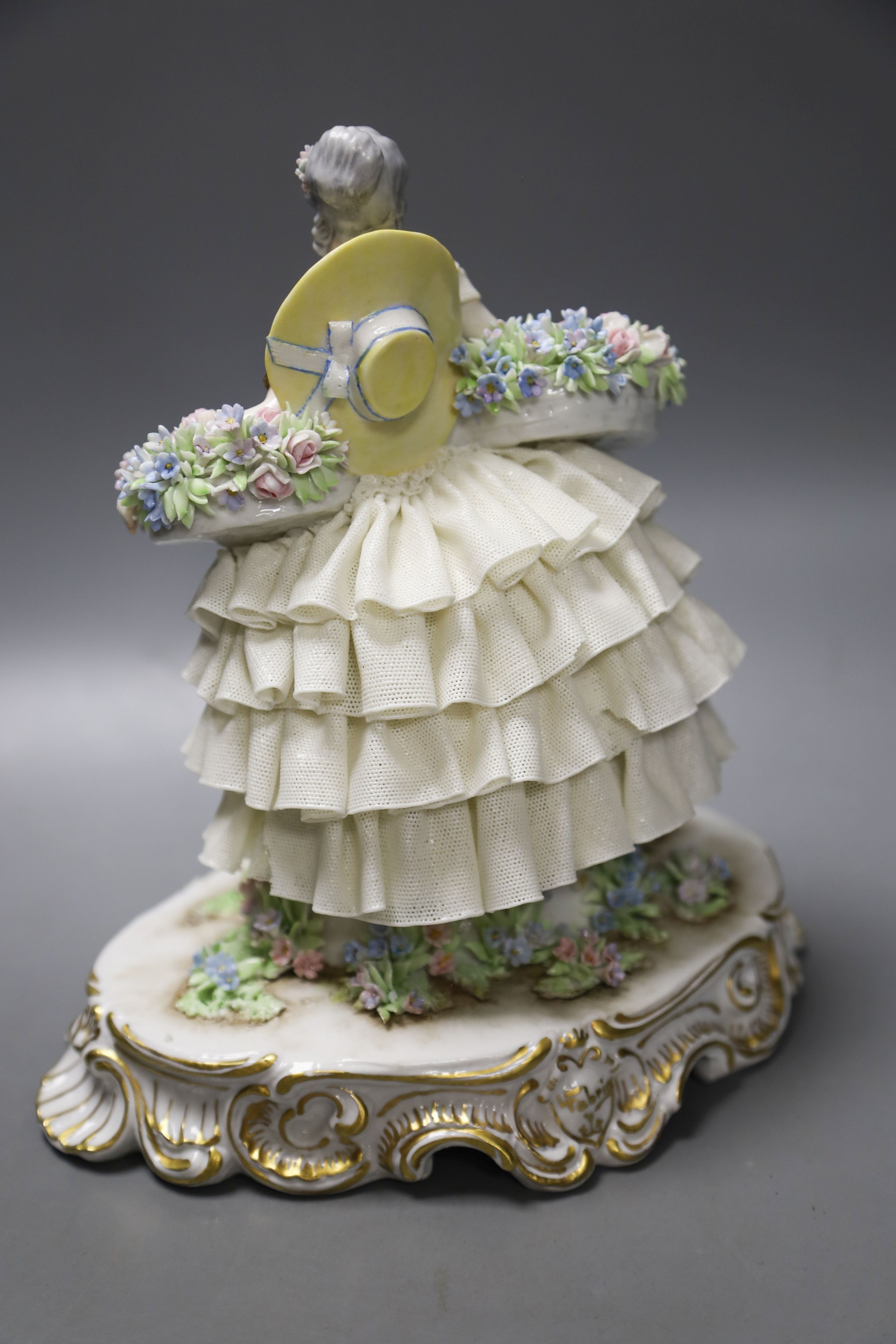 A Luigi Fabris porcelain figure of a lady wearing a crinoline dress, holding baskets of flowers, and two other figural groups (3)